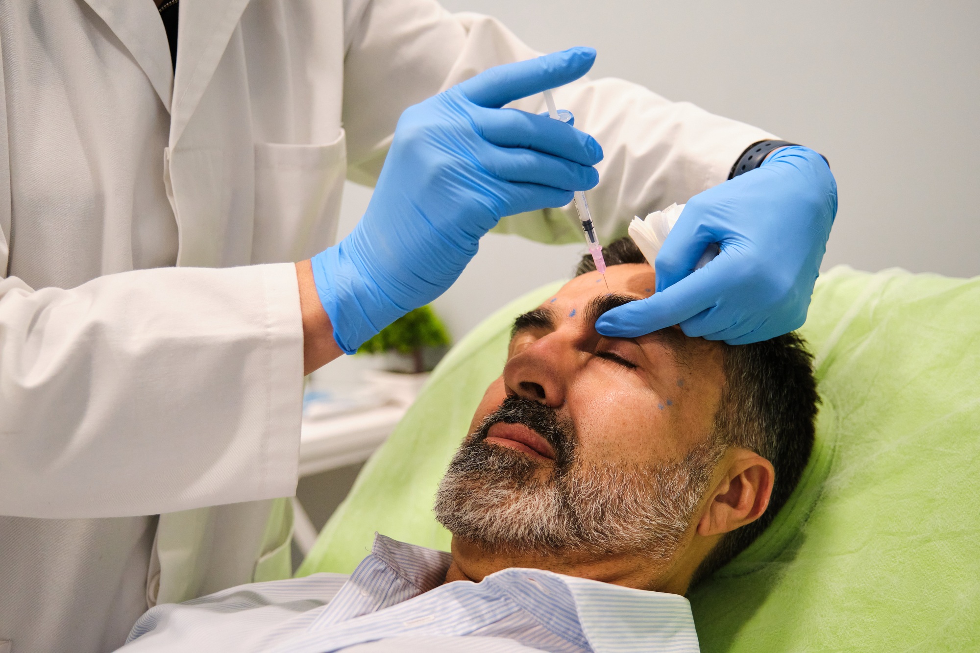 A man is getting Botox for forehead wrinkles by a aesthetic doctor in a clinic.