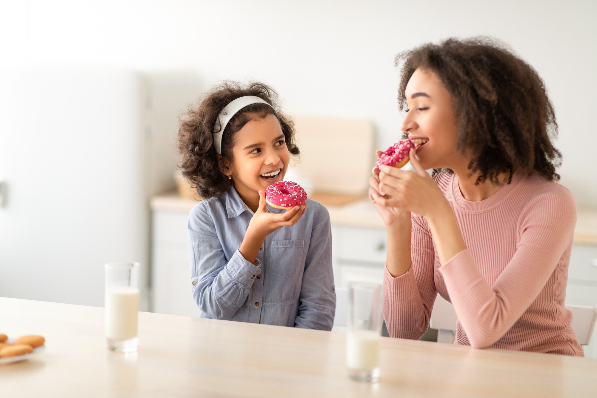 Black mother and daughter eating sweets in kitchen