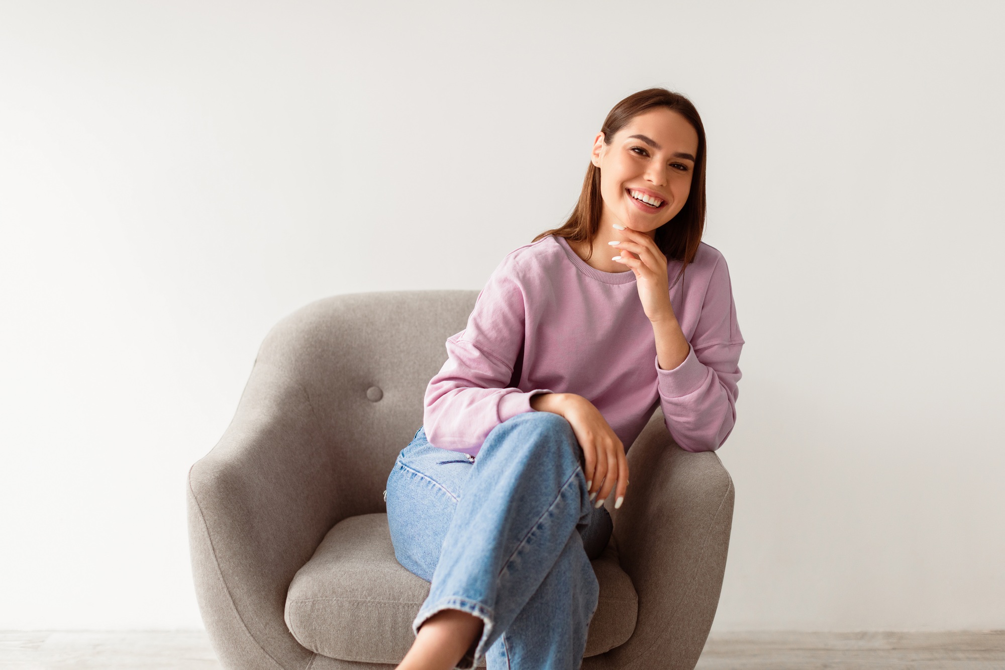 Happy person. Young Caucasian woman sitting in armchair, looking at camera, posing on white studio
