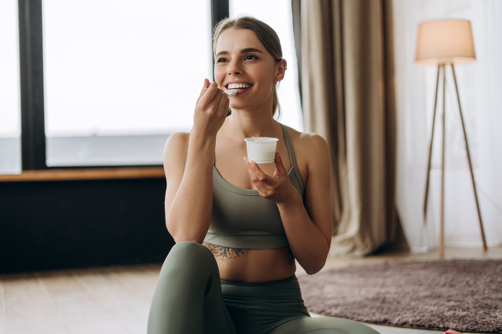 Happy smiling sportswoman enjoying yogurt after training at home